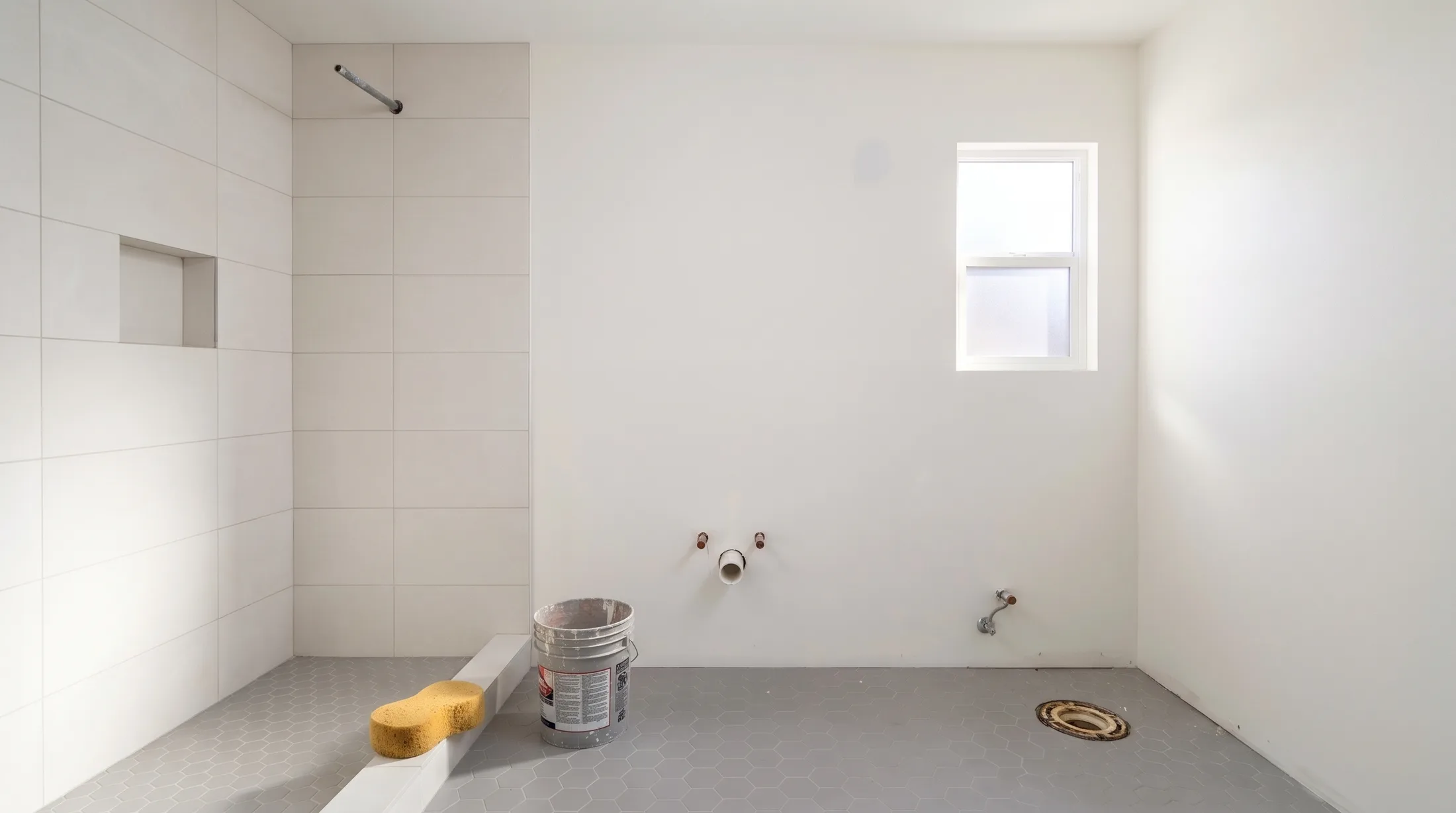 The same room with the shower tile and the hexagon floor finished, plumbing stubs waiting where the vanity and toilet go