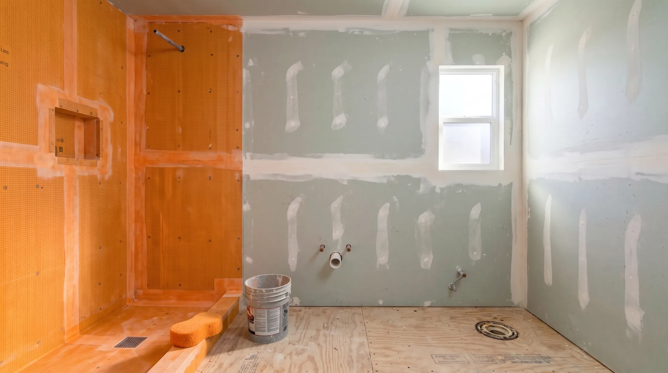 The same bathroom today: the shower and niche covered in orange waterproofing membrane, the walls boarded and taped